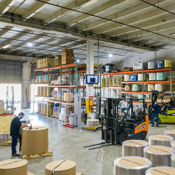 Entrepôt avec palettes, chariots élévateurs et employés manipulant des marchandises.