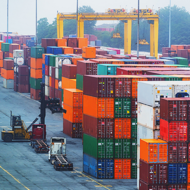Fret maritime avec conteneurs colorés empilés sur le quai. Engins de manutention présents.
